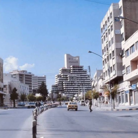 A street in Shmeisani, Amman, in the 1980s, with office buildings and a stepped high-rise in the background